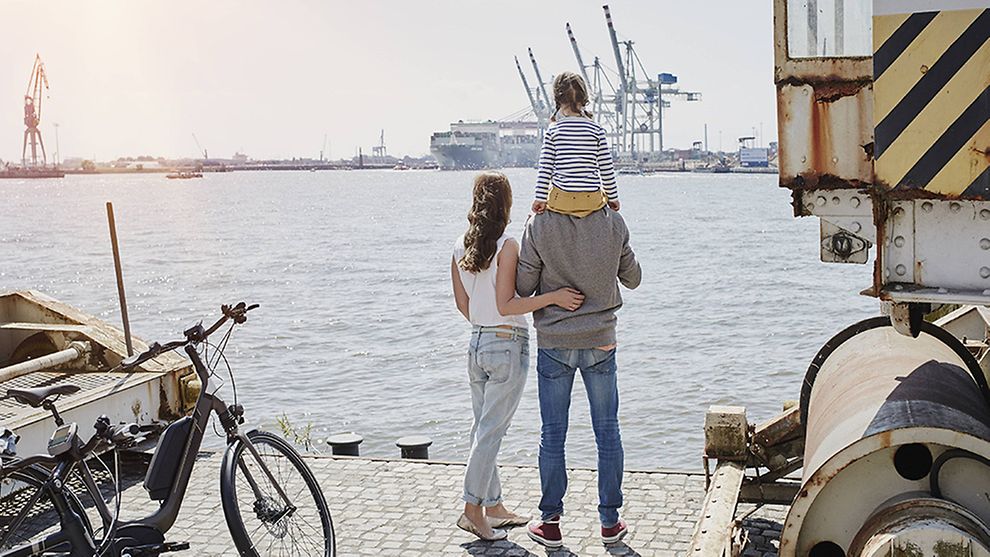 a man carries his kid and stand next to his wife at port of Hamburg